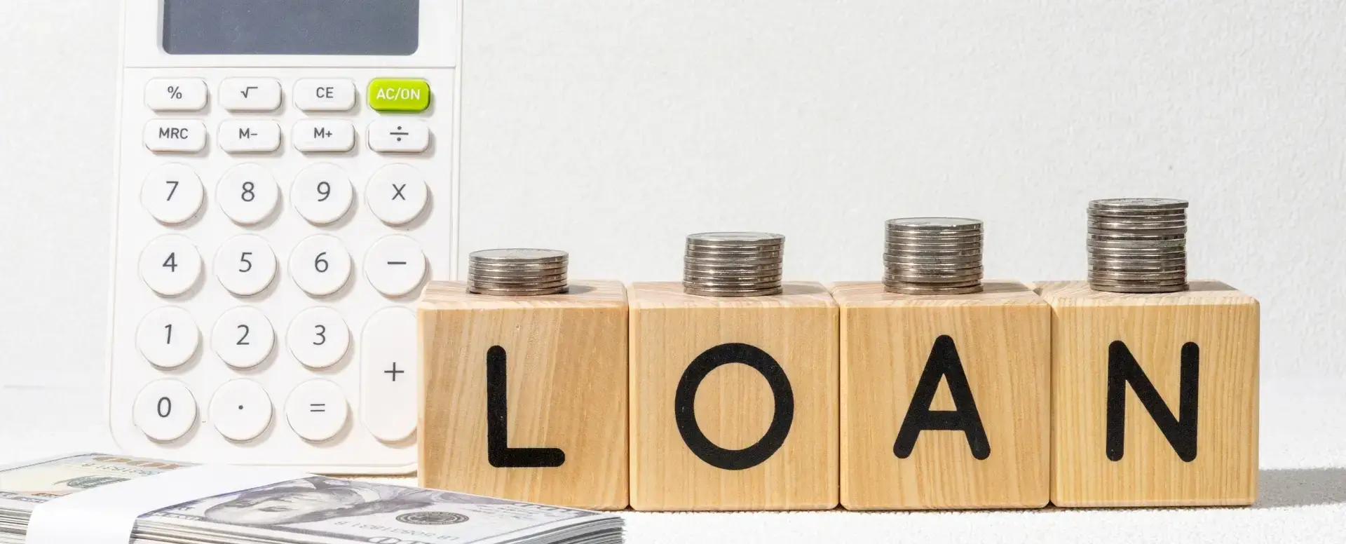 Calculator and stacks of coins on wooden blocks spelling LOAN, highlighting home loans for first-time home buyers.