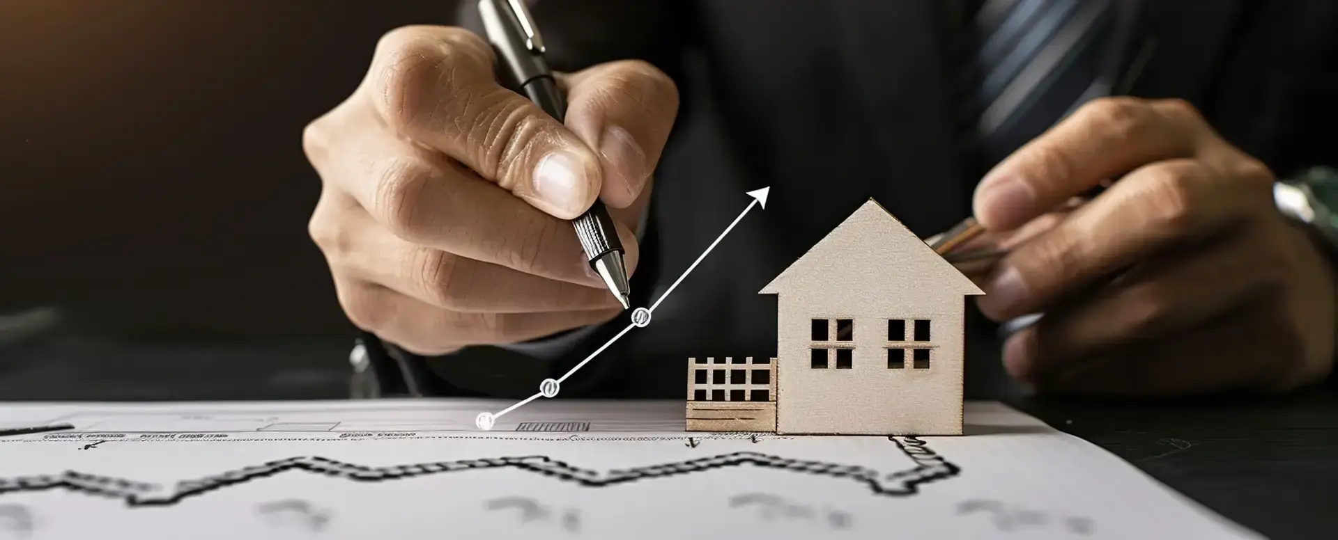 A person draws a rising graph near a house model, highlighting real estate growth for first-time home buyers.