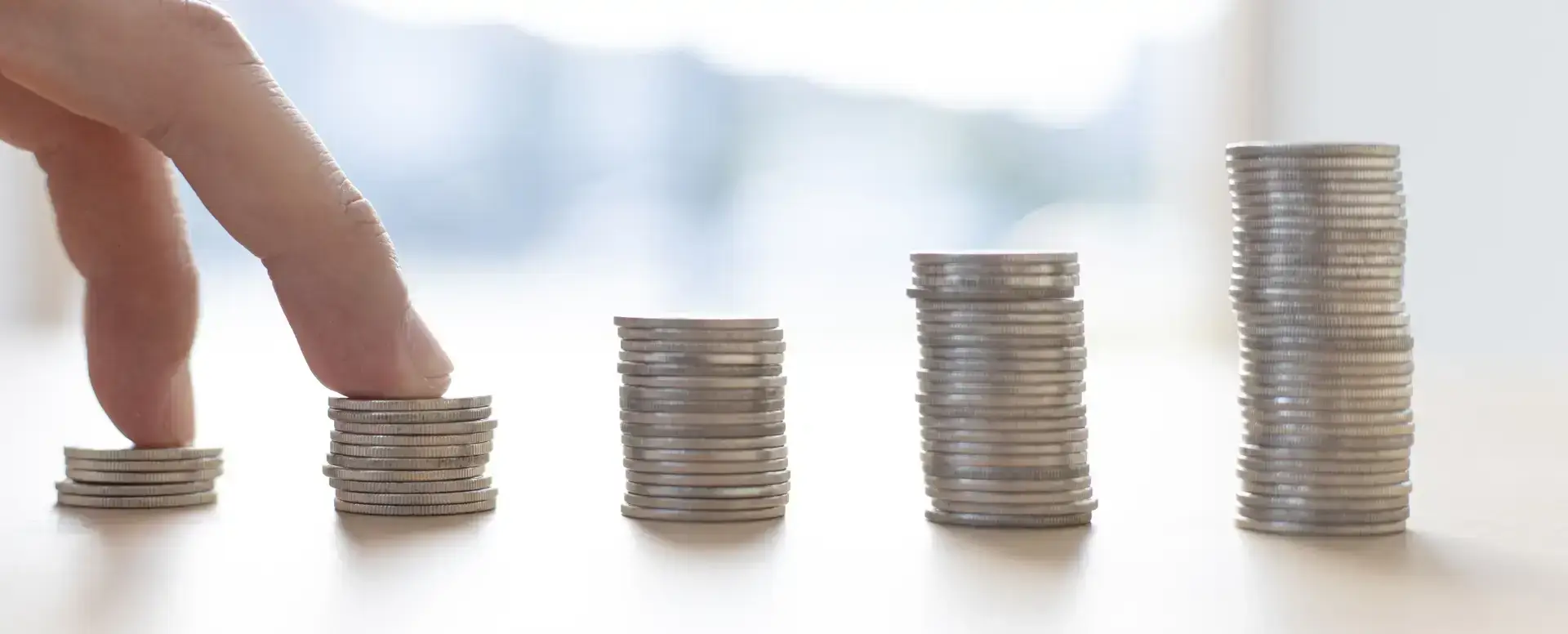 A hand stacking coins in ascending order, symbolizing savings for first-time home buyers or purchase home loans.