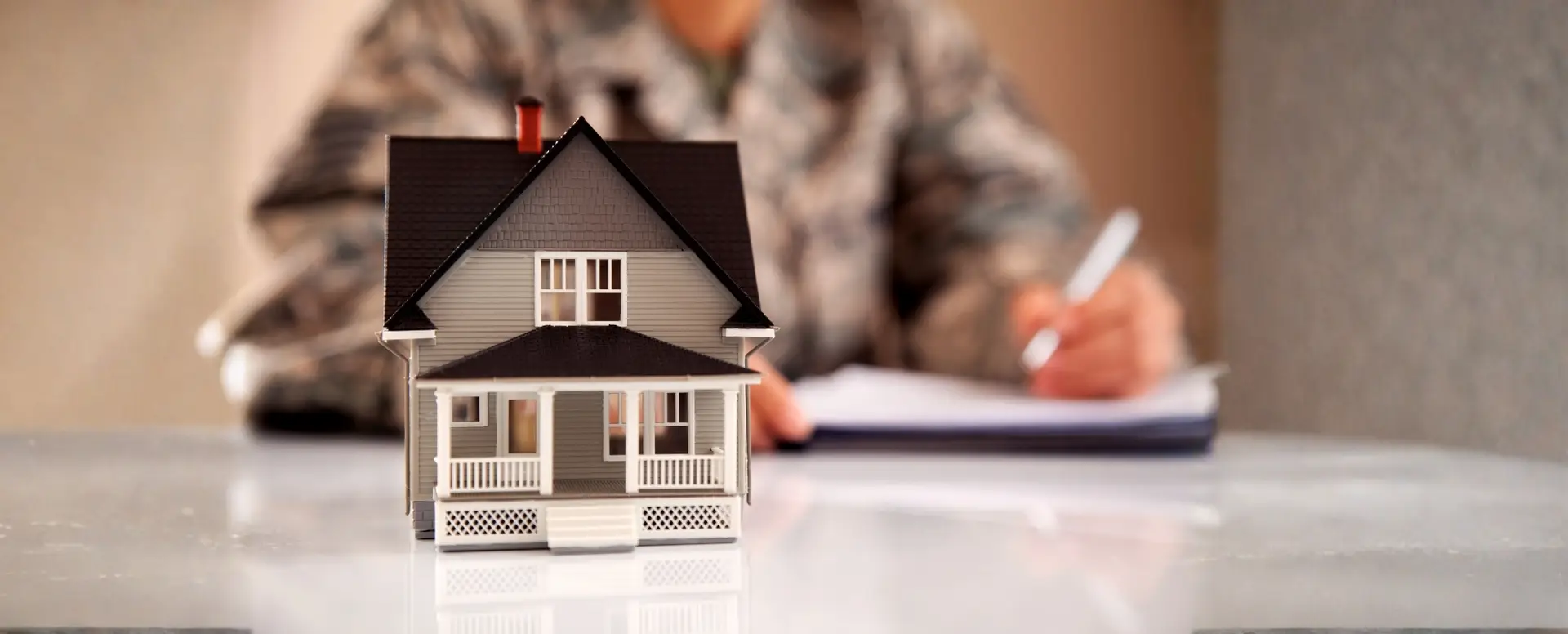 A small model house sits on a table as a mortgage lender writes in uniform in the blurred background.