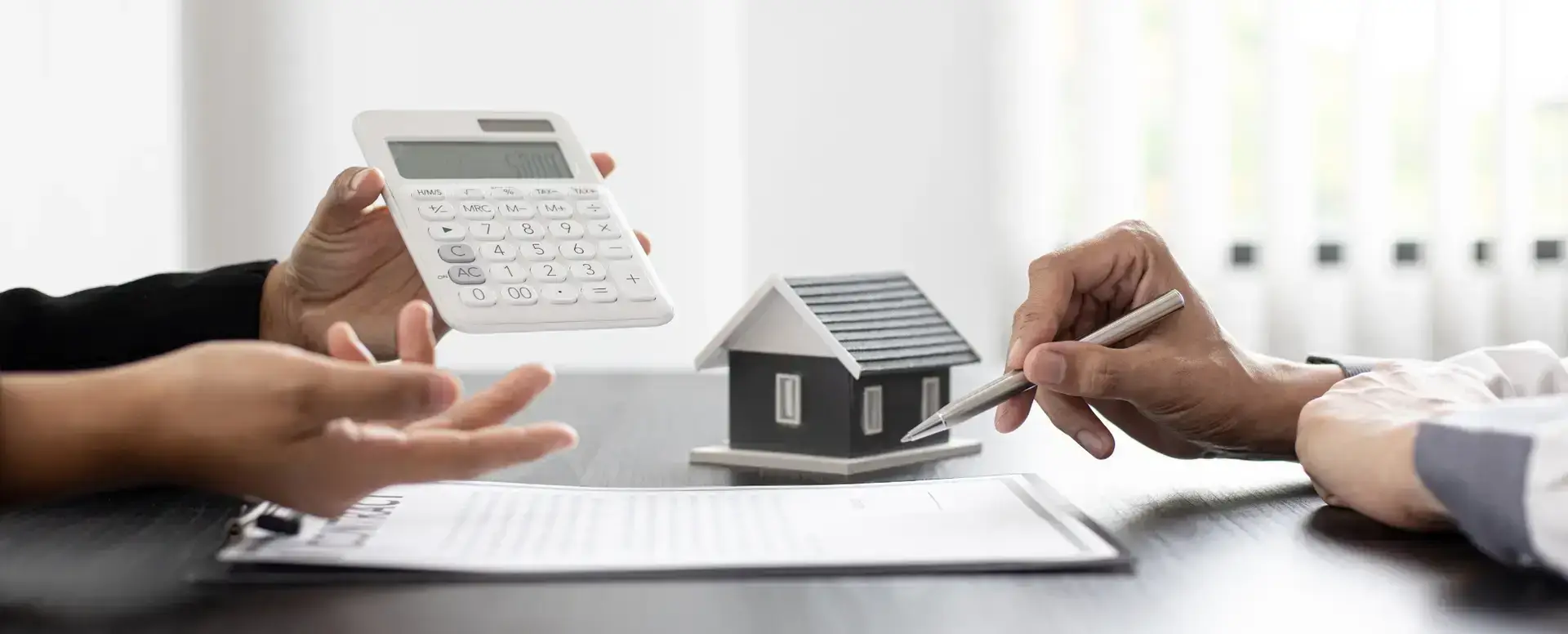 Two people discuss paperwork, calculator, and house model—ideal scene for first-time home buyers or home loans advice.