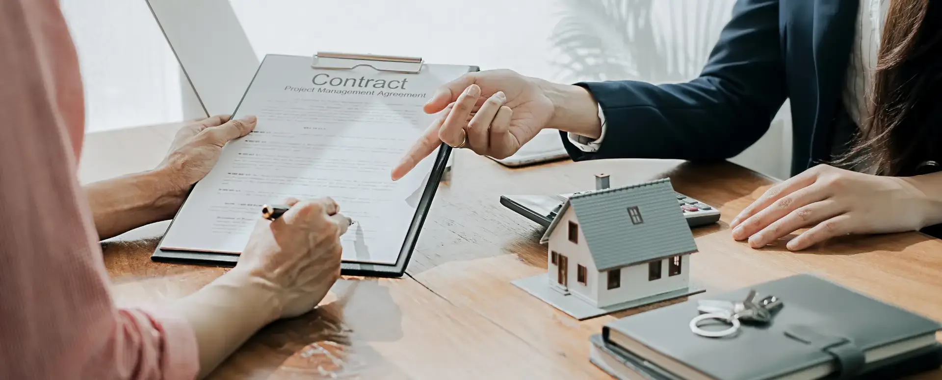 Two people sign a contract at a desk with keys and documents—ideal for first-time home buyers or mortgage refinance.