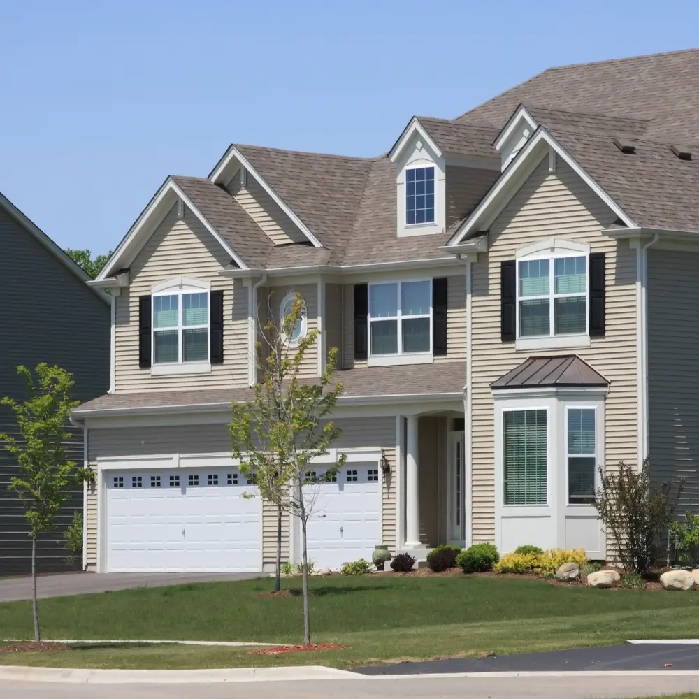 Two-story suburban house ideal for first-time home buyers, with beige siding, black shutters, and a three-car garage.