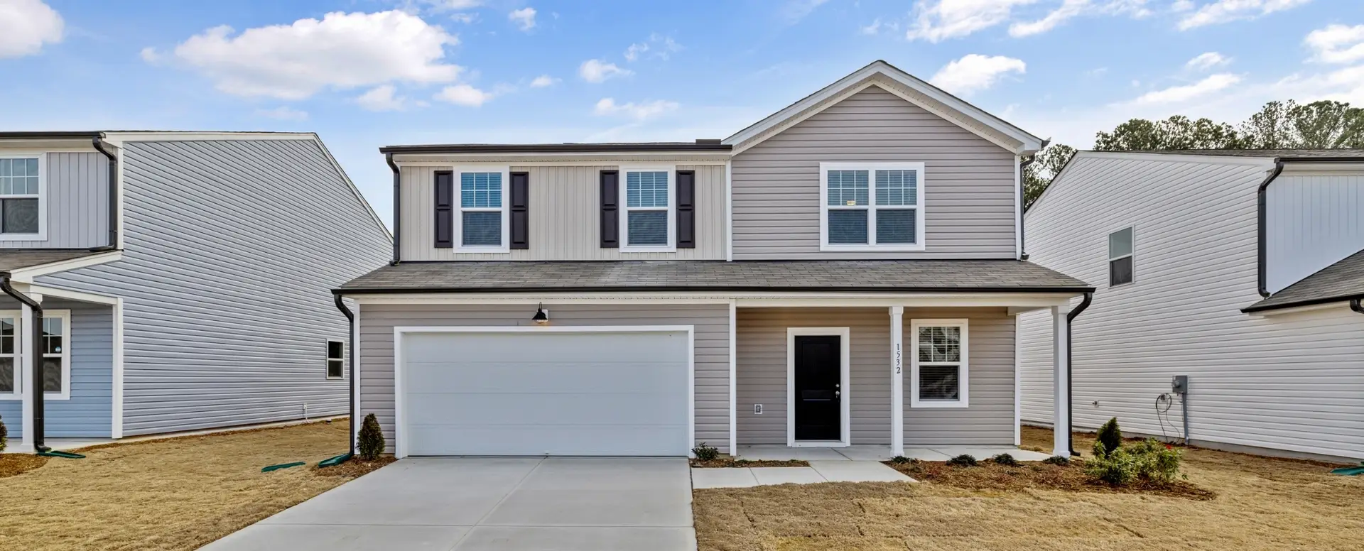 Two-story suburban house with a porch and gray siding—ideal for first-time home buyers on a newly landscaped lawn.
