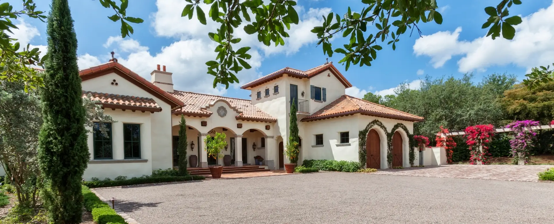A large Mediterranean-style house, perfect for home loans, with arched doorways and a spacious driveway under a blue sky.
