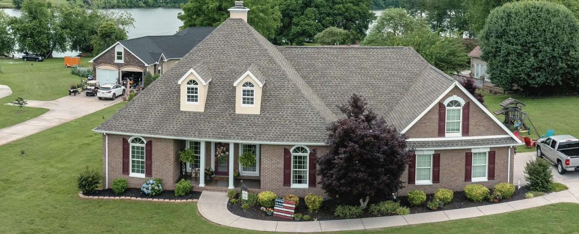 A brick suburban house with a large front yard—ideal for first-time home buyers—overlooks a scenic lakeside view.