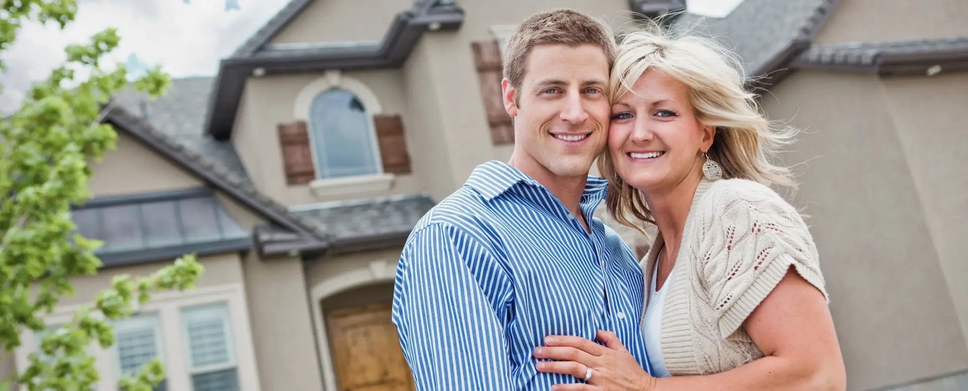 Smiling couple standing close together in front of their new home—perfect for first-time home buyers.