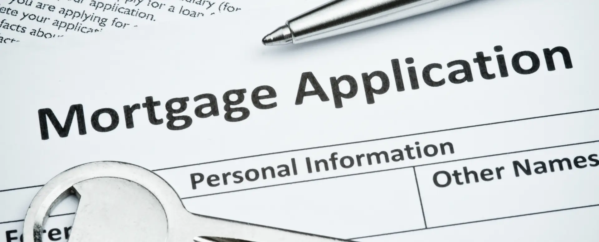 Close-up of a mortgage application form with a pen, metal key, and home loans details for first-time home buyers.