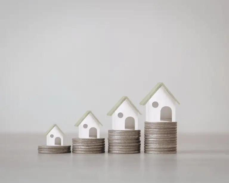 Four small model houses sit atop coin stacks, representing rising property value or smart moves like mortgage refinance.