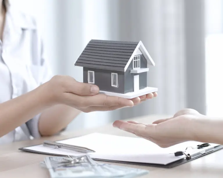 A person hands over a model house, with money and documents displayed—perfect for home loans or a mortgage lender.