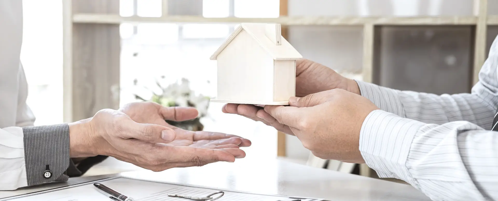 Two people exchange a model house at a desk, symbolizing a real estate deal with a mortgage lender.