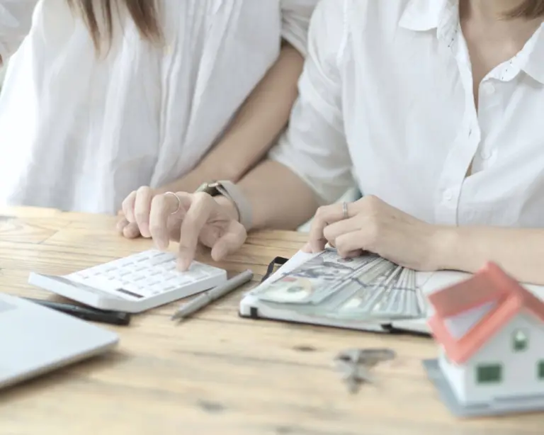Two people in white shirts review documents and use a calculator, possibly first-time home buyers meeting a mortgage lender.