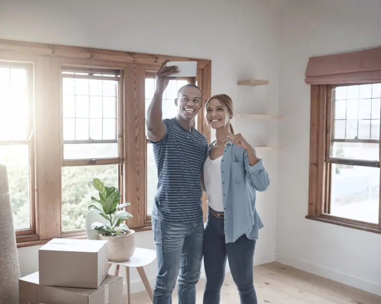 Smiling couple takes a selfie with moving boxes, celebrating their new keys thanks to home loans.