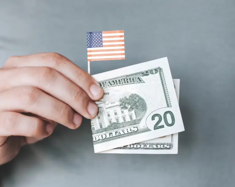 A hand holds US dollar bills, a small American flag—perfect for home loans or mortgage refinance themes against gray.