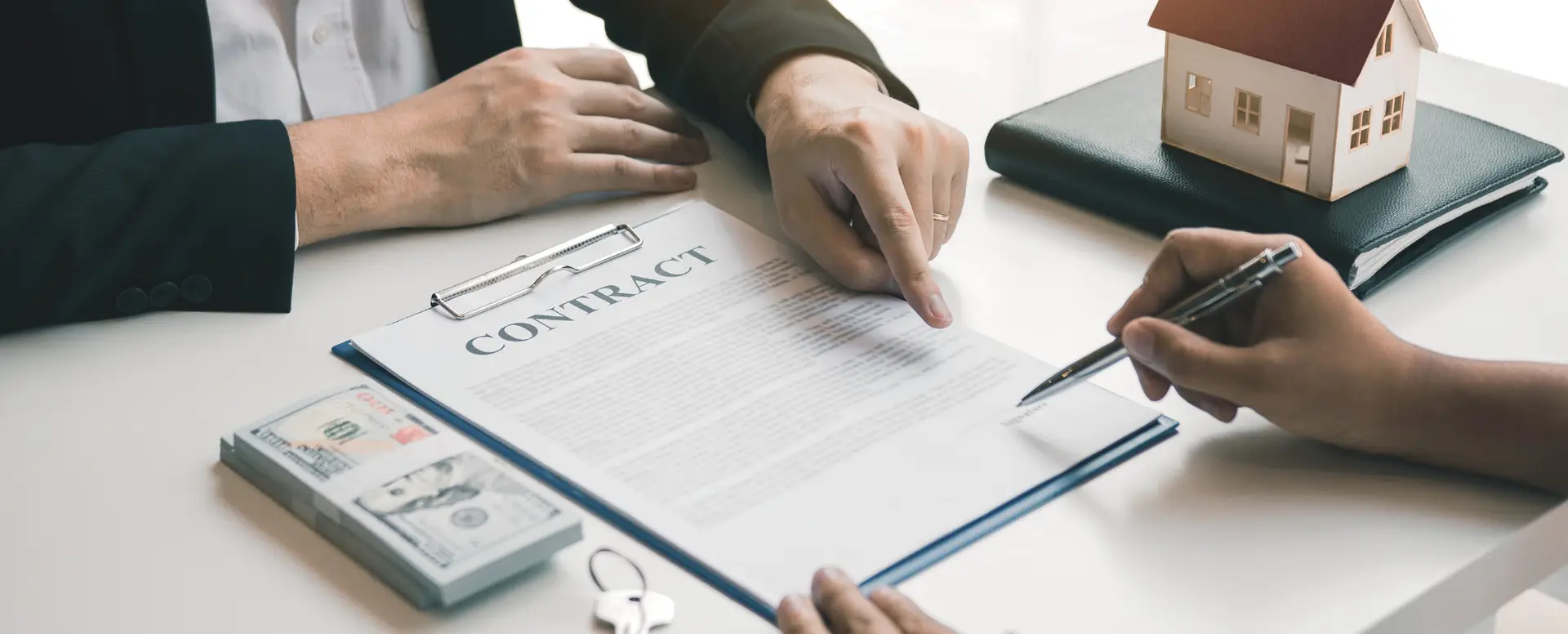 Two people sign a contract at a desk with money, keys, and a house model—consulting a mortgage lender.