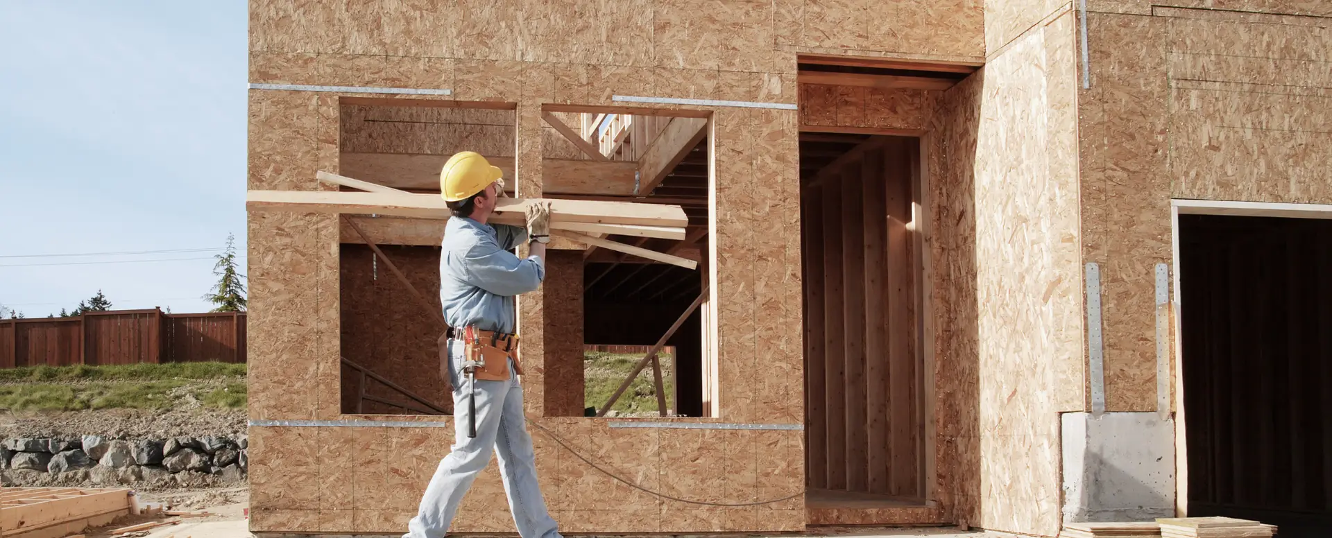 Construction worker in a yellow hard hat carrying wooden planks—let a mortgage lender help fund your dream home build.