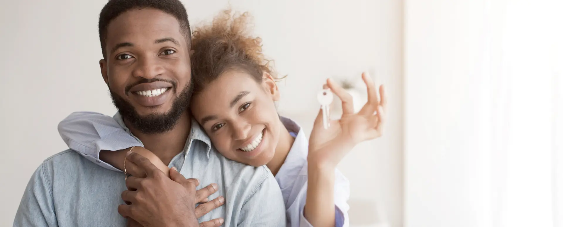 Smiling couple hugging, holding house keys, celebrating their new home with the help of purchase home loans.