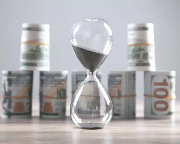 An hourglass with black sand stands before US dollar bills, highlighting the urgency in choosing a mortgage lender.