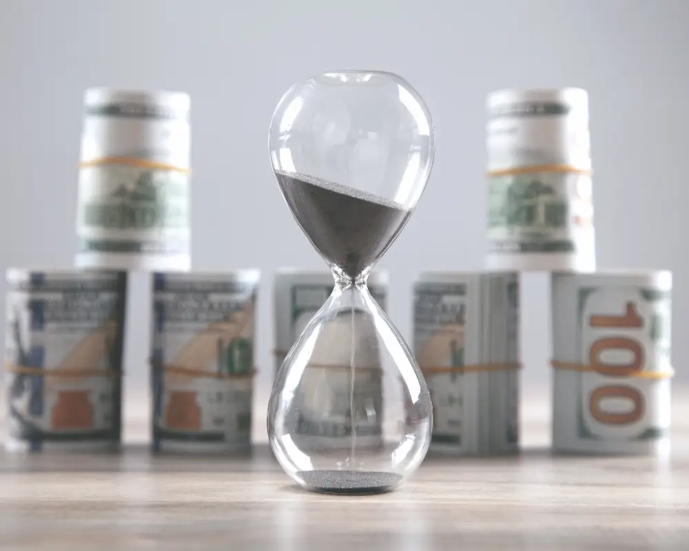 An hourglass with black sand stands before US dollar bills, highlighting the urgency in choosing a mortgage lender.