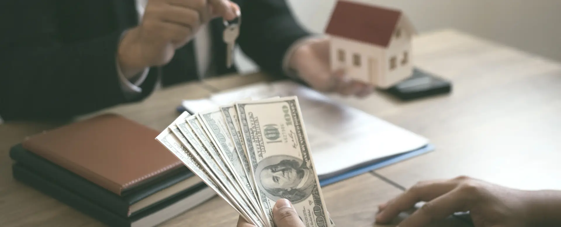Person holding cash, another handing over house keys with a model house—perfect for first-time home buyers.