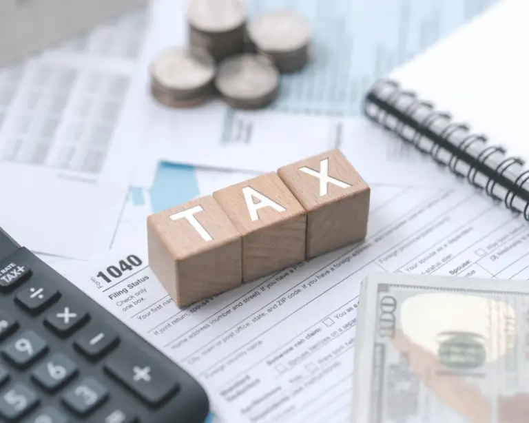 Wooden blocks spelling TAX on tax forms, with a calculator and coins—ideal for those considering mortgage refinance.