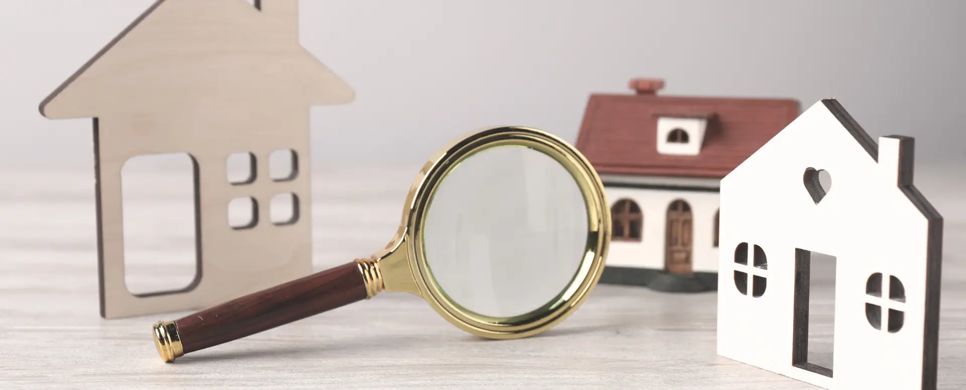 A magnifying glass is placed among three small wooden house models, symbolizing the search for home loans.
