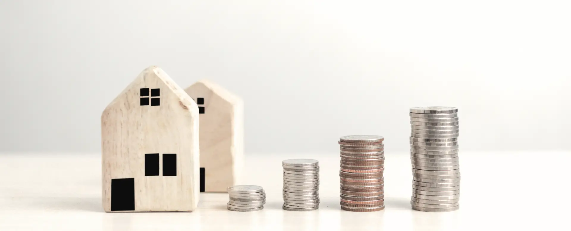 Two small wooden house models beside four coin stacks, symbolizing options for first-time home buyers.