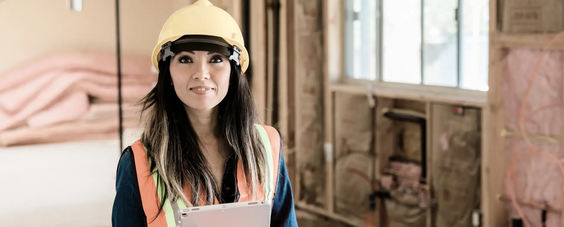 Woman in a hard hat and vest holding a tablet, inspecting building progress for construction loans.