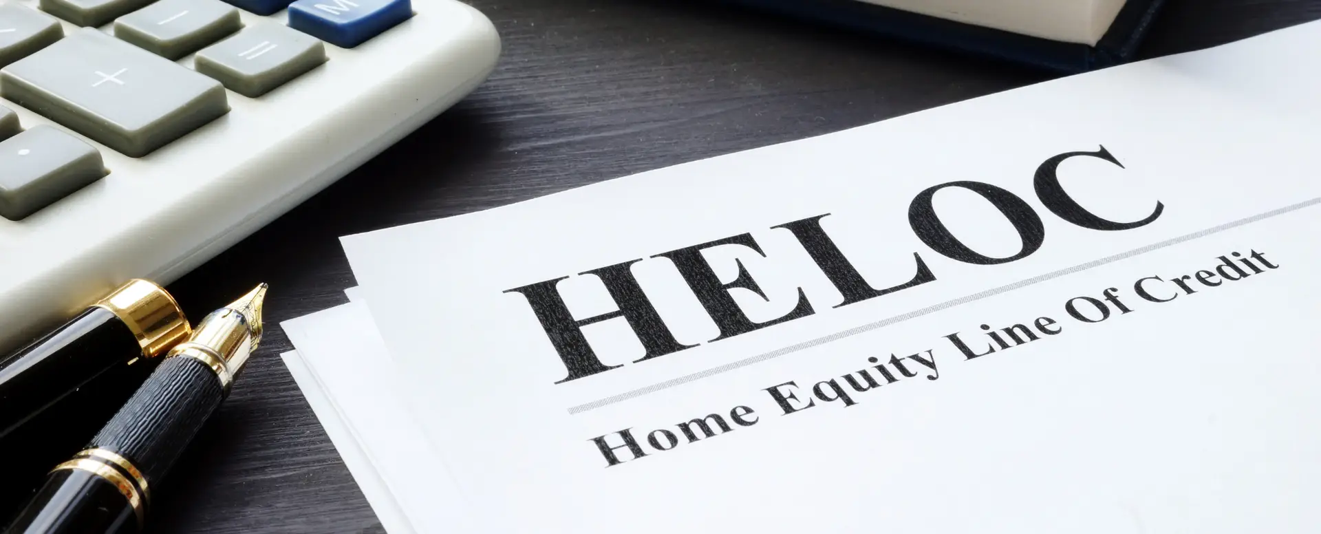 A document titled HELOC Home Equity Line of Credit lies on a desk with a pen, calculator, and mortgage refinance form.