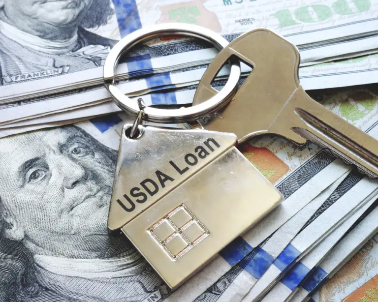 A house-shaped keychain labeled USDA Loan with keys, perfect for first-time home buyers, on hundred-dollar bills.