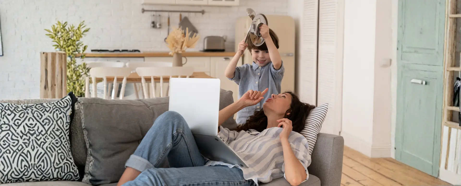 A woman relaxes with her laptop while her child plays nearby—perfect moments for first-time home buyers.