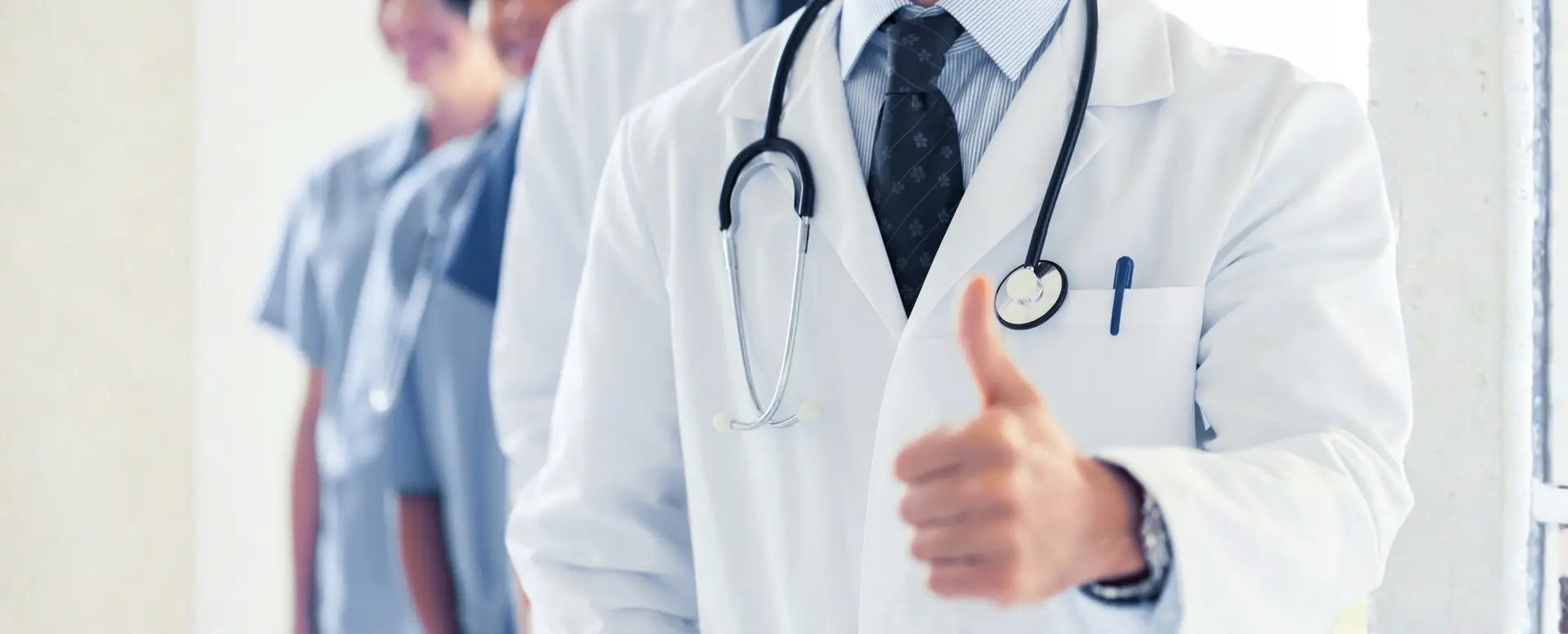A doctor in a white coat gives a thumbs up, supporting first-time home buyers with staff in the background.