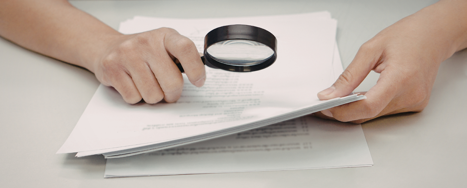 A person examines home loan documents with a magnifying glass on a desk.