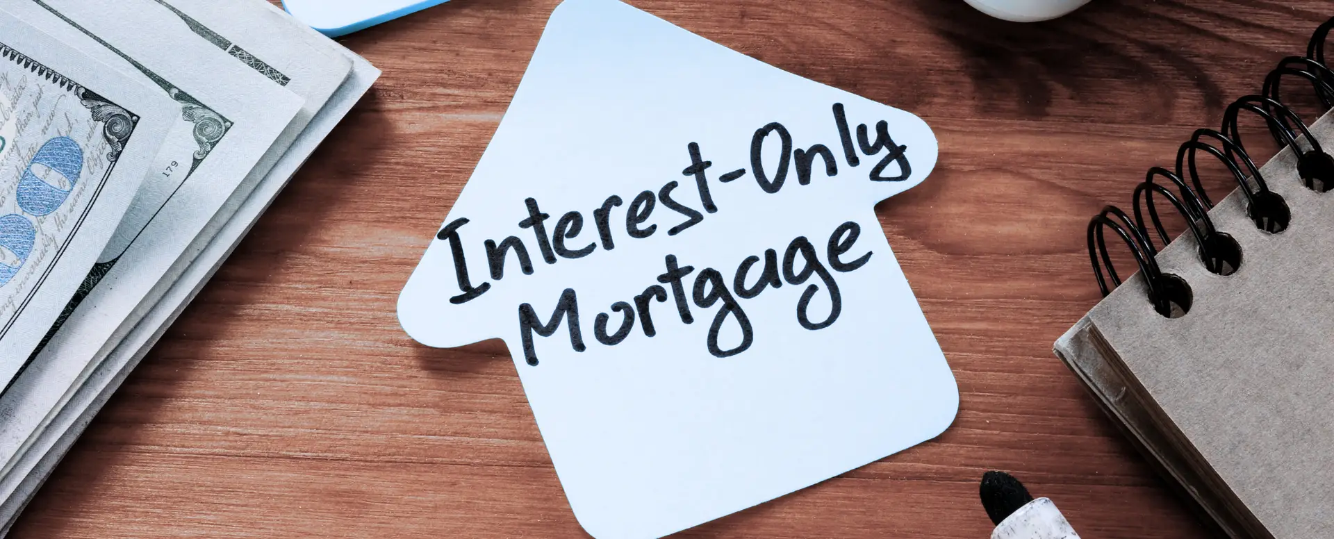 A house-shaped paper labeled Interest-Only Mortgage on a desk with money, ideal for first-time home buyers.