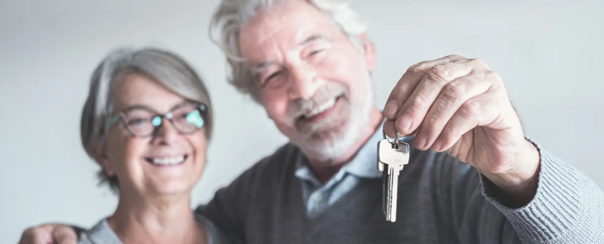 Smiling older couple holding a key, celebrating with their mortgage lender as first-time home buyers.