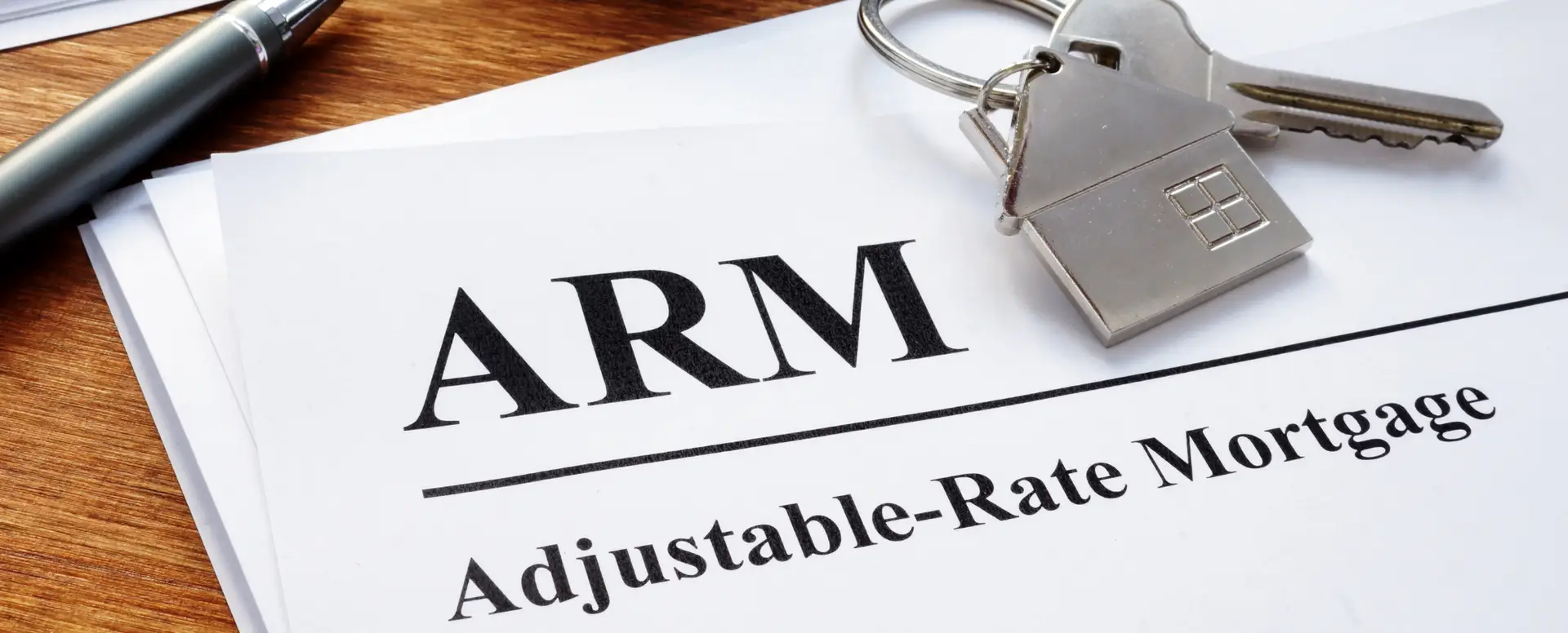 A document labeled ARM Adjustable-Rate Mortgage, ideal for first-time home buyers, with a house keychain and pen on wood.