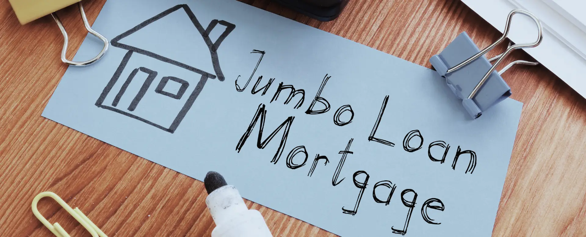 Paper with a house drawing and "Jumbo Loan Mortgage" showing options for home loans on a desk with office supplies.
