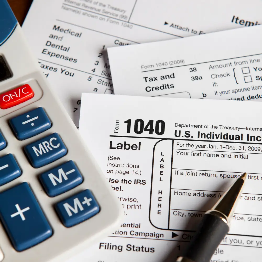 A calculator, tax forms, and a pen on a desk, highlighting first-time home buyers preparing for income tax returns.