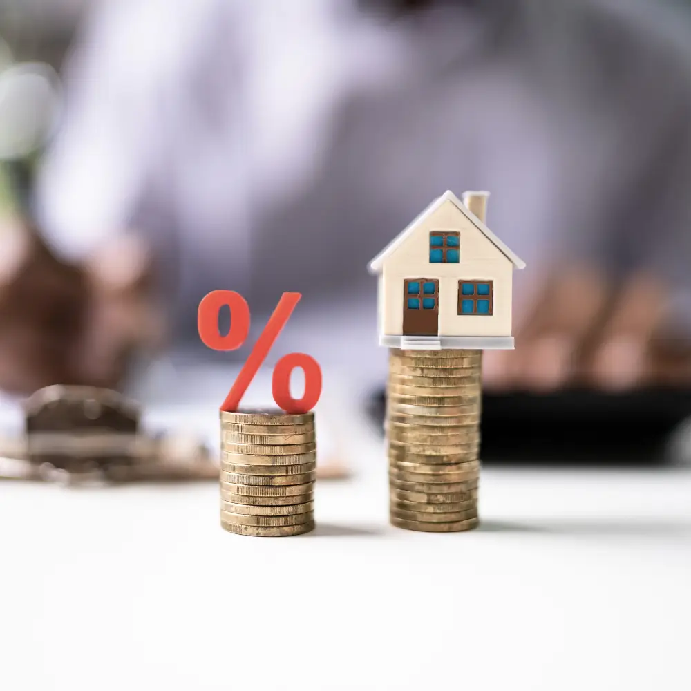 Stacks of coins with a red percent sign and a small house model symbolize home loans and mortgage interest rates.