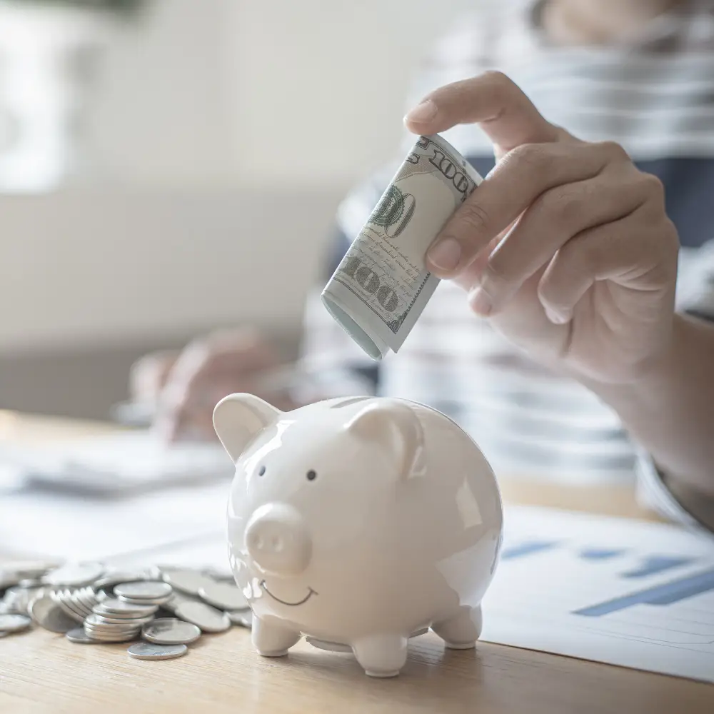 Person putting a rolled-up dollar bill into a piggy bank, saving for home loans—ideal for first-time home buyers.