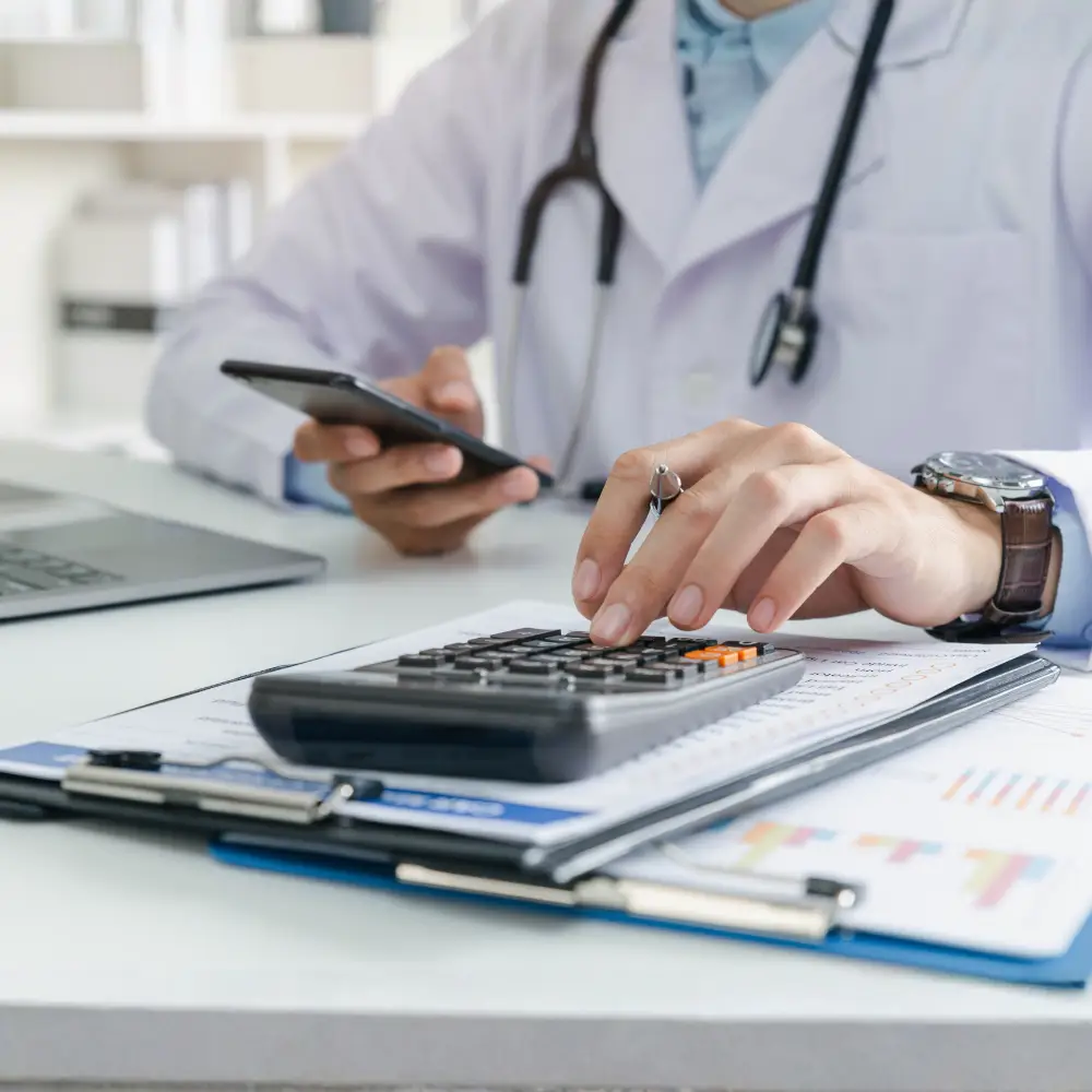 A doctor reviews documents and uses a smartphone, planning finances for construction loans at the desk.